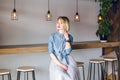 Shy sweet girl with blonde hair and pink lips sitting in a coffee shop with wooden chairs and table playing with her Royalty Free Stock Photo