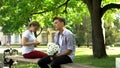 Shy teen with flowers sitting next to lady, surfing net on phone, hesitation