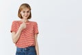 Shy and timid cute elder daughter standing insecure over gray background in striped t-shirt, pointing right while