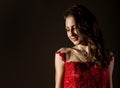Shy woman lowered her eyes smiles timid. Girl in elegant red dress on a dark background. free space for your text