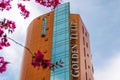 Golden Tulip Ana Tower hotel with its panoramic elevator, as seen from the street, framed by pink flowers