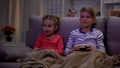 Siblings covered with plaid enjoying video game, playing at night, using console