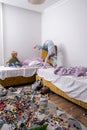 siblings having fun, laughing, boy and girl jumping on bed in messy childrens room, kids playing among the many toys at Royalty Free Stock Photo