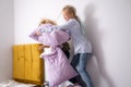 siblings having fun, laughing, boy and girl play pillow fight in messy childrens room, kids playing among the many toys Royalty Free Stock Photo