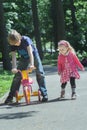 Siblings playing with pink and yellow kids tricycle on park tarmac footpath Royalty Free Stock Photo