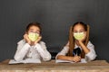 Siblings, schoolchildren are sitting at a school desk over black wall l in medical protective masks. Quarantine at school. Back to Royalty Free Stock Photo