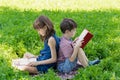 Siblings are sitting back-to-back on the lawn in the park and reading books. Royalty Free Stock Photo