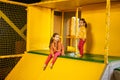 Siblings sliding at yellow playground park. Sisters in active entertaiments