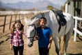 Siblings standing with white horse in the ranch