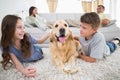 Siblings stroking dog on rug while parents relaxing on sofa