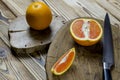 Sicilian oranges and knife with black knob rests on a wooden board, which stands on a wood table