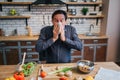 Sick adult man sneezing to white napkin. He stand at table in kitchen. Desk full of colorful healthy vegetables and Royalty Free Stock Photo