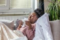 Sick African American woman with headache sitting under the blanket. Sick woman covered with a blanket lying in bed with seasonal Royalty Free Stock Photo