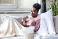 Sick African American woman with headache sitting under the blanket. Sick woman covered with a blanket lying in bed with seasonal Royalty Free Stock Photo