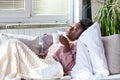 Sick African American woman with headache sitting under the blanket and drinking hot beverage. Sick woman covered with a blanket Royalty Free Stock Photo