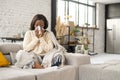 Sick African-American woman sitting covered with blanket on the couch and blowing nose Royalty Free Stock Photo