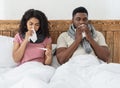 Sick african couple sitting in bed, measuring fever, sneezing noses Royalty Free Stock Photo
