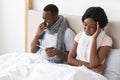 Sick african couple sitting in bed, measuring fever, sneezing noses Royalty Free Stock Photo