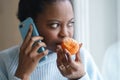 Sick afro woman trying to sense smell of half fresh tangerine orange talking on phone. Covid-19 Royalty Free Stock Photo