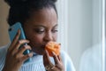 Sick afro woman trying to sense smell of half fresh tangerine orange talking on phone. Covid-19 Royalty Free Stock Photo