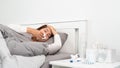 Sick Asian woman with cold sleeping on bed at home with high fever suffering from insomnia and medicine in foreground Royalty Free Stock Photo