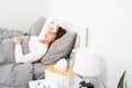 Sick Asian woman with cold sleeping on bed at home with high fever suffering from insomnia and medicine in foreground Royalty Free Stock Photo