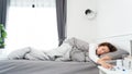 Sick Asian woman lying in bed take medicines pills and glass of water from bedside table to relieve symptoms Royalty Free Stock Photo