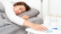 Sick Asian woman lying in bed take medicines pills and glass of water from bedside table to relieve symptoms Royalty Free Stock Photo