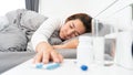 Sick Asian woman lying in bed take medicines pills and glass of water from bedside table to relieve symptoms Royalty Free Stock Photo