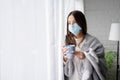 Sick Asian woman quarantined and wearing face mask from covid at home She held a glass of water near the window of her house and