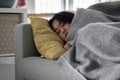 Sick Asian woman sleeping on sofa under blanket at home, recovering from flu Royalty Free Stock Photo