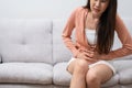 Sick Asian Woman Suffering From Acute Abdominal Pain in the abdomen due to menstruation period, PMS. Sitting On Couch, Royalty Free Stock Photo