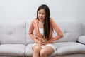 Sick Asian Woman Suffering From Acute Abdominal Pain in the abdomen due to menstruation period, PMS. Sitting On Couch, Royalty Free Stock Photo