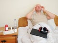 Sick bald man in his bed, medicine and tablet with headphones in his reach, hands at head, concept head ache, flu, corona virus