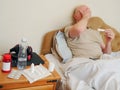 Sick bald man in his bed with thermometer, pills and water by his side. Concept flu, corona virus treatment