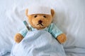 Sick bear is wearing patient clothes. lying in bed with fever, a fever-reducing gel on his forehead and at the temperature temple