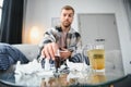 Sick bearded man who has bad cold or seasonal flu sitting on couch at home. Guy with fever wearing warm plaid shivering Royalty Free Stock Photo