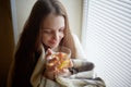 Sick beautiful woman with colds and drinks hot tea with lemon sitting by the window in a country house in winter Royalty Free Stock Photo