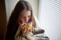 Sick beautiful woman with colds and drinks hot tea with lemon sitting by the window in a country house in winter Royalty Free Stock Photo