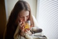 Sick beautiful woman with colds and drinks hot tea with lemon sitting by the window in a country house in winter Royalty Free Stock Photo