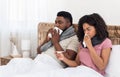 Sick black couple sitting in bed, measuring fever, sneezing noses Royalty Free Stock Photo