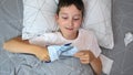 A sick boy lying in bed and cutting a hateful mask with scissors and tear it onto two pieces