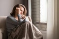 Sick brunette woman with headache having cold and flu sneezing sitting on the couch in the living room near window. Royalty Free Stock Photo