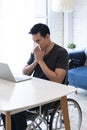 Sick Business entrepreneur in wheelchair sneezing in the home office. Disabled Sick Young Man on Wheelchair at Home. Young man in Royalty Free Stock Photo