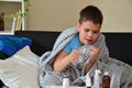 Sick child boy lying in bed with a fever, resting at home. a boy with a cold, treated. medicines, throat nose spray Royalty Free Stock Photo