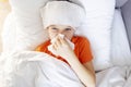 Sick child boy is lying in bed with high fever and blowing his nose, resting at home Royalty Free Stock Photo