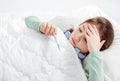 Sick child with flu fever laying in bed and  holding thermometer Royalty Free Stock Photo