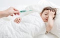 Sick child with flu fever laying in bed and mother holding thermometer Royalty Free Stock Photo