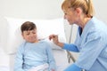 Sick child lying in bed in hospital room and nurse giving him medicine with spoon