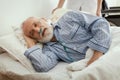 Sick elderly man wearing blue pajama lying in bed at nursing home Royalty Free Stock Photo